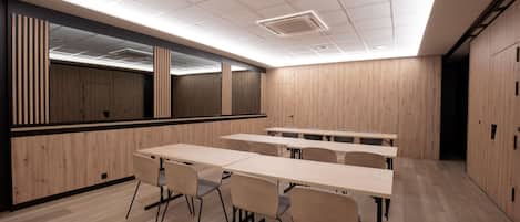 Un salón de conferencias con paredes de paneles de madera, techo alto con iluminación empotrada y varias mesas y sillas.