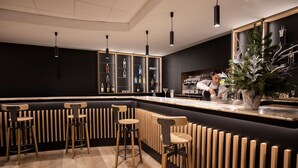 Un área de bar moderna con taburetes de madera, una barra negra y una planta grande en maceta.