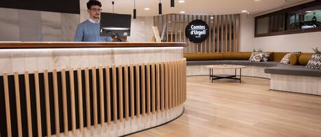 A modern reception area with a curved reception desk, a seating area with cushions, and a sign reading "Comtes d'Urgell".