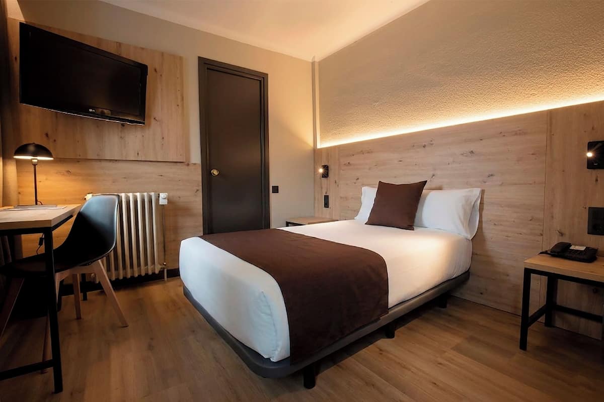 Hotellihuone, jossa on sänky, työpöytä, tuoli, televisio ja ovi.