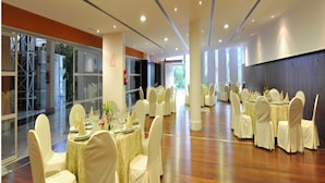 Un amplio salón de banquetes con mesas y sillas redondas, ventanas grandes y un suelo de madera pulida.