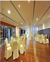 Un amplio salón de banquetes con mesas y sillas redondas, ventanas grandes y un suelo de madera pulida.