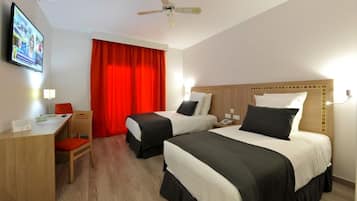 A hotel room with two beds, a desk, a chair, a television, and a ceiling fan.