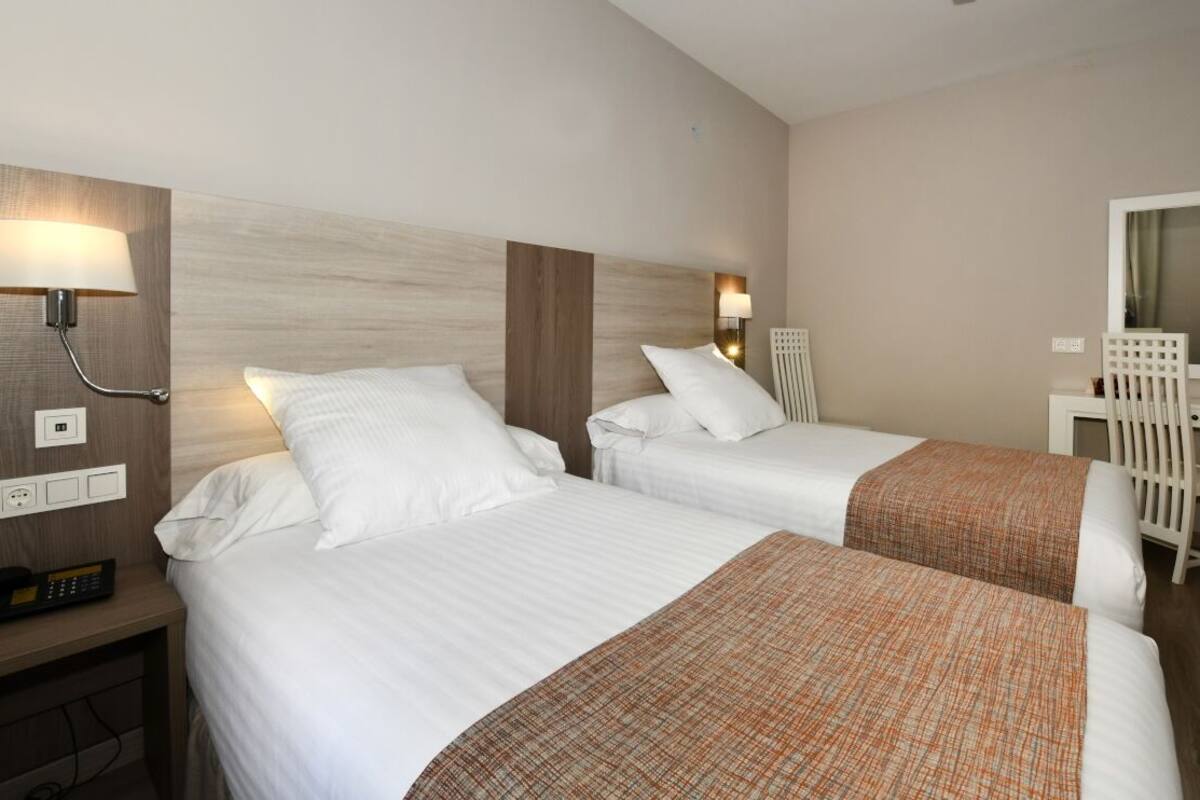 A hotel room with two beds, a desk, a chair, a lamp, and a mirror.