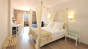 Una cama con dosel y cortinas, una mesita de noche con lámpara, y una silla.