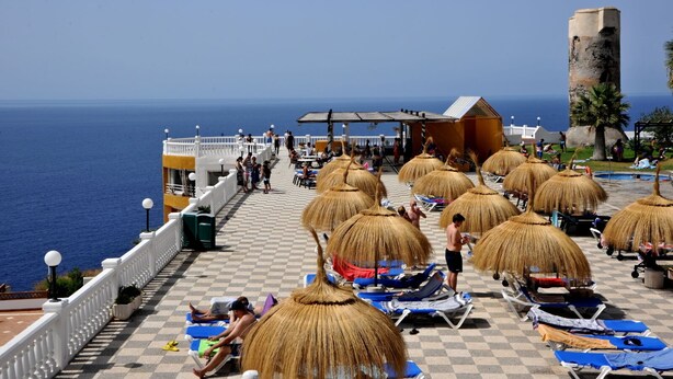 Un complejo turístico frente al mar con sombrillas de paja, tumbonas y vistas al océano.