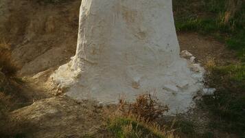 Una estructura blanca y cilíndrica con una pequeña abertura en la parte superior, ubicada en una colina cubierta de hierba con un sendero de tierra que lleva hacia ella.