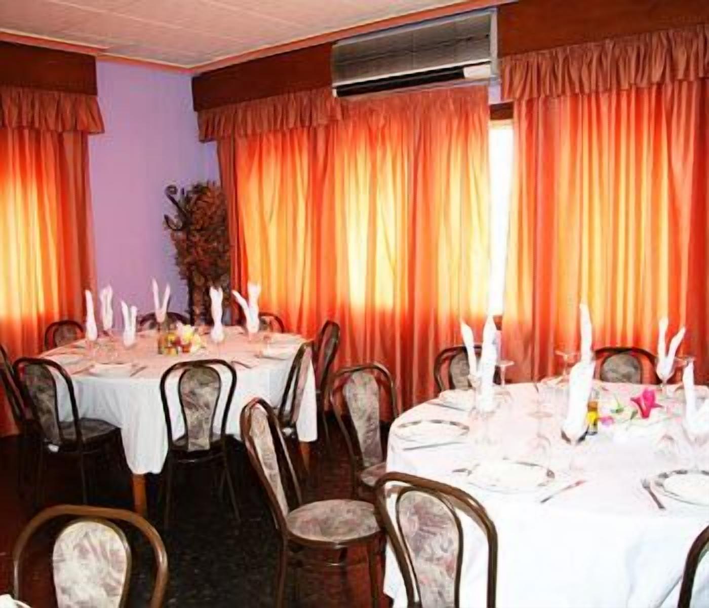 Zona pranzo con tavoli apparecchiati per quattro, ognuno con tovaglia bianca, candele e centrotavola floreale.
