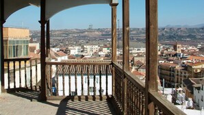 Ein Balkon mit Holellentrailsse, der auf eine Stadtlandschaft mit Gebäuden und Hügeln im Hintergrund blickt.