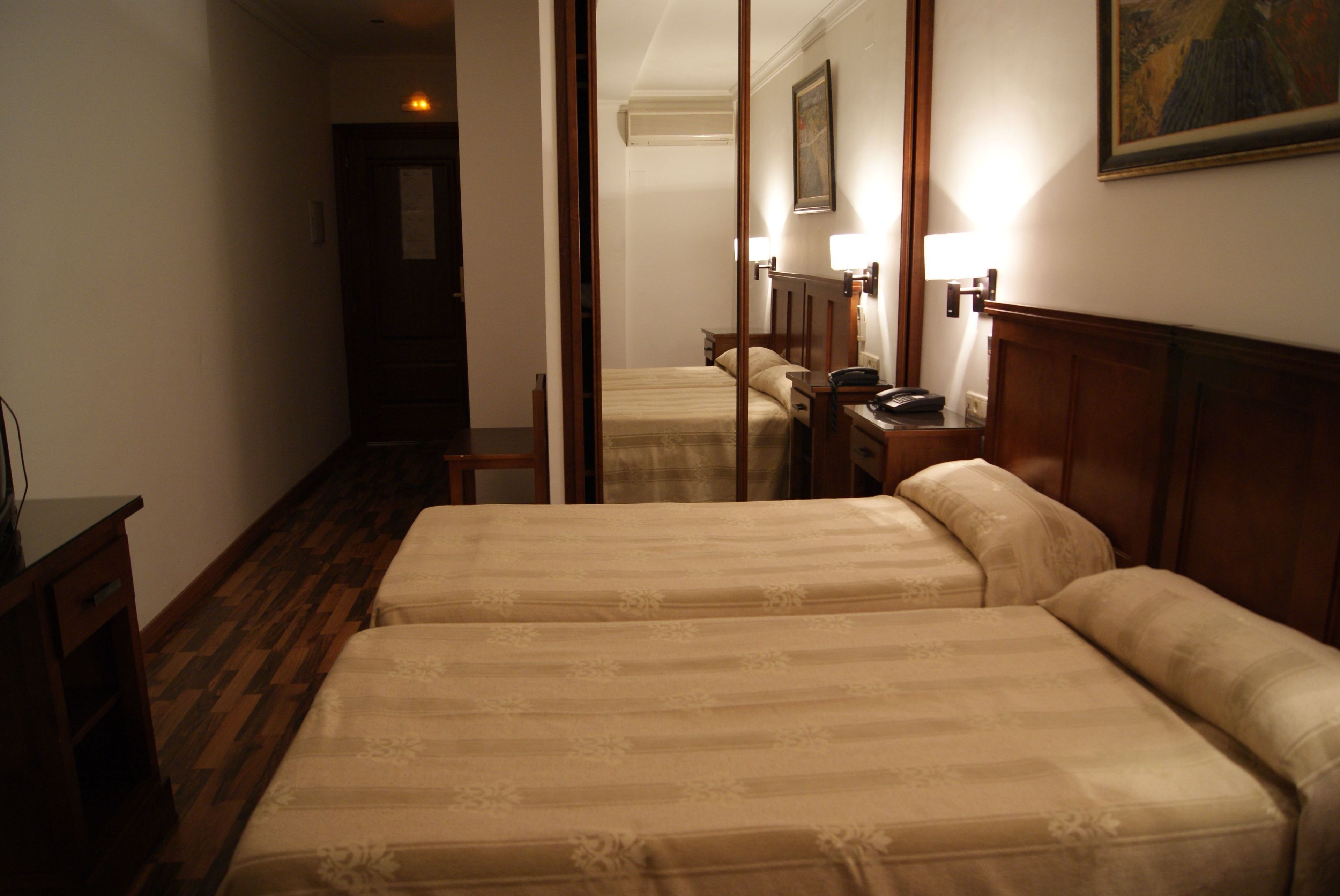 A hotel room with two beds, wooden flooring, a desk, and a nightstand.