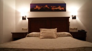 Ein Hotelzimmer mit einem großen Bett, zwei Nachttischen, einem Wandbild einer Stadtansicht und zwei Wandlampen.