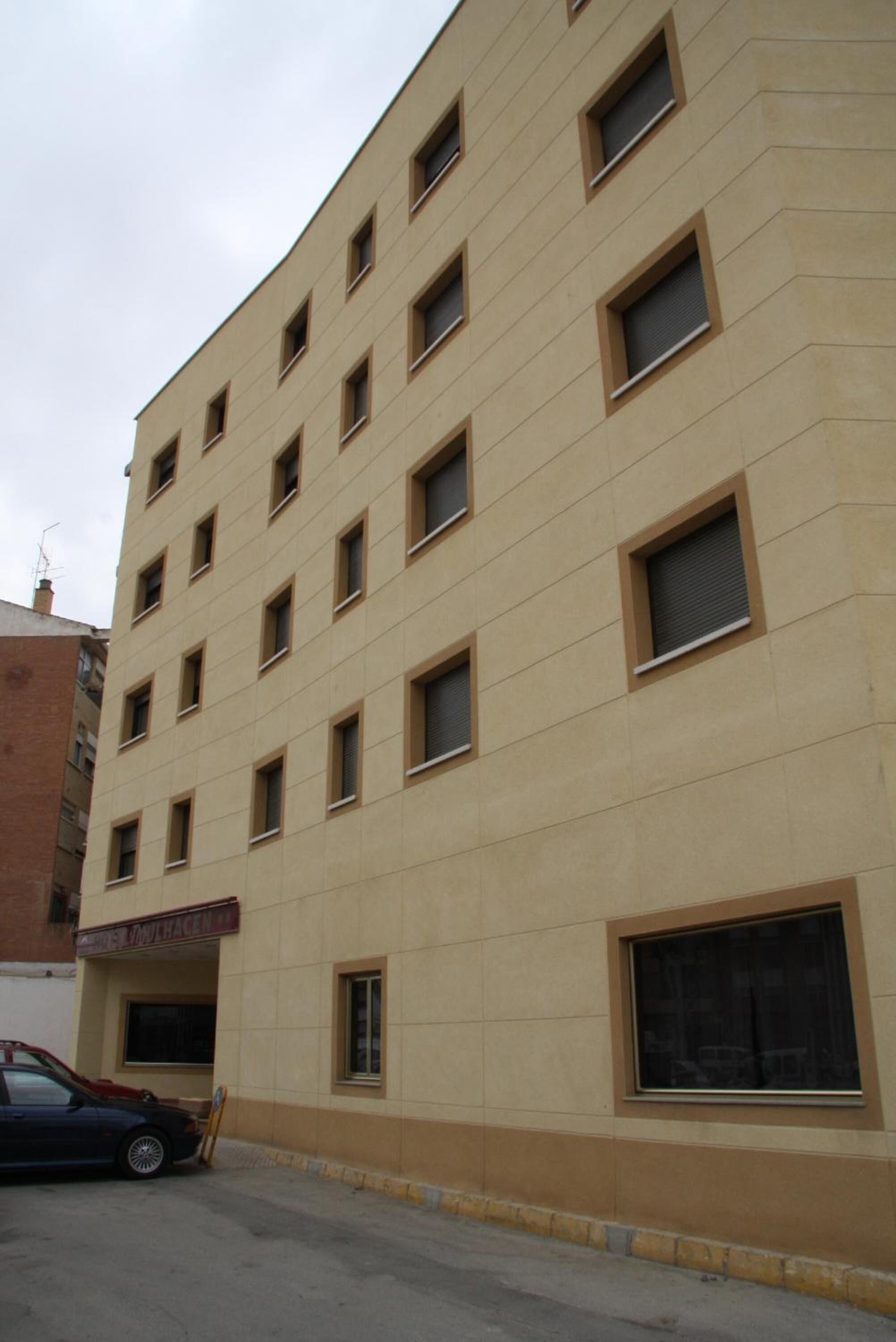 Un edificio de varios pisos con fachada color beige, varias ventanas y una entrada visible con un letrero.