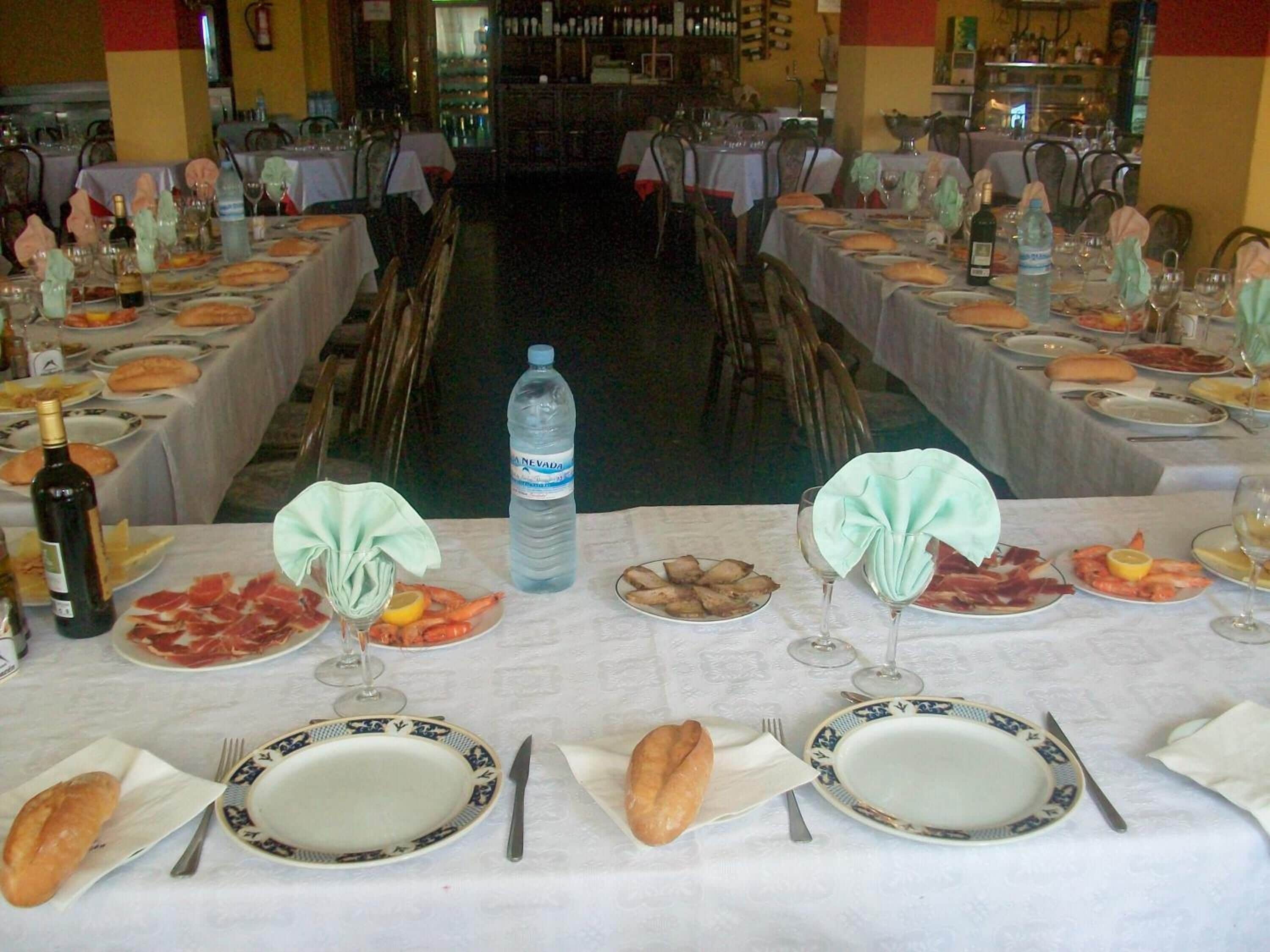 Ein Restaurant mit mehreren gedeckten Tischen, Essensplatten, Weingläsern und Wasserflaschen.