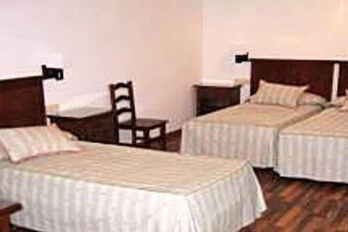 Ein Zimmer mit zwei Einzelbetten, Holz-Kopfteilen, einem kleinen Holzstuhl und einem Nachttisch mit Lampe.