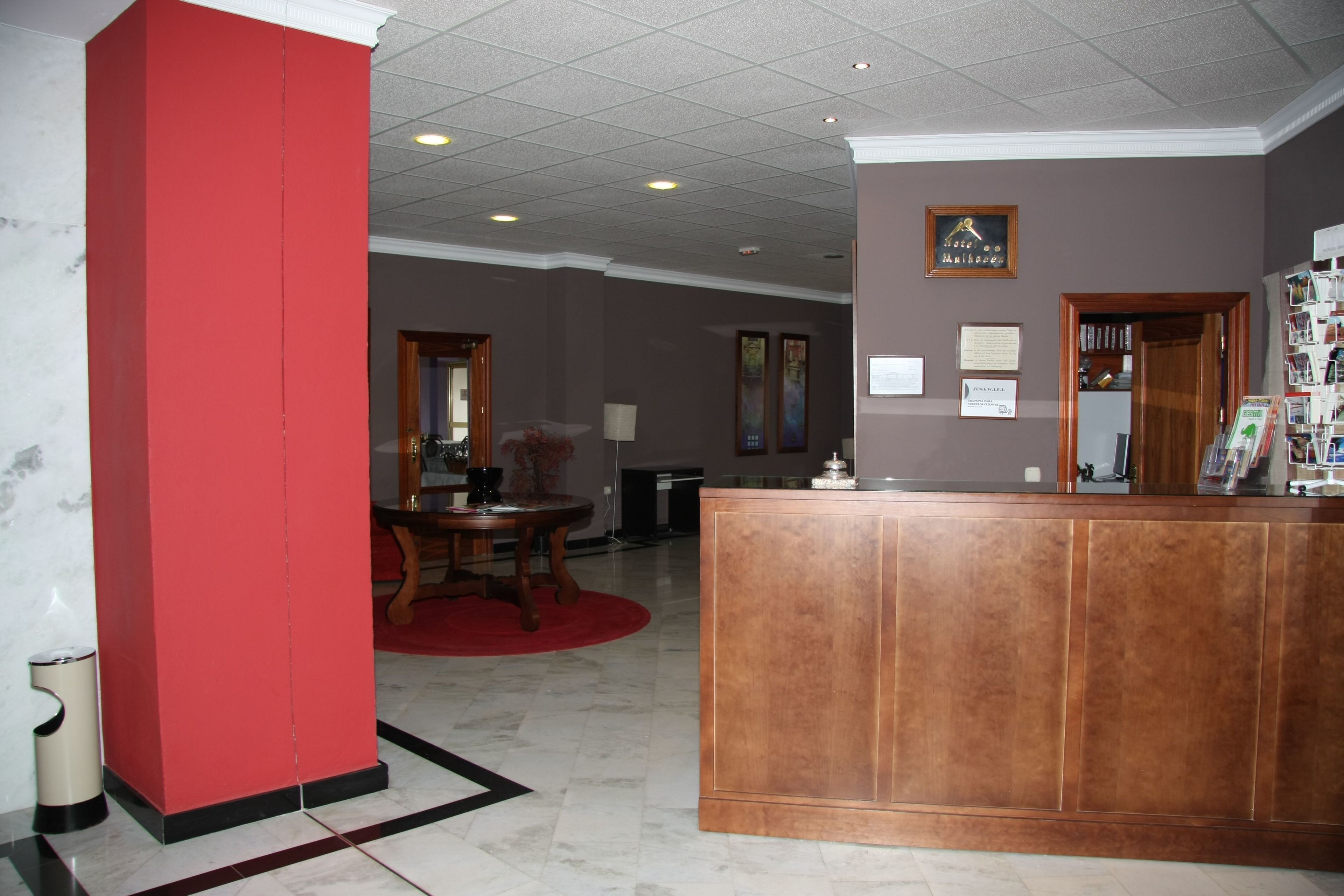 A reception area with a wooden reception desk, a red pillar, a marble floor, and a framed certificate on the wall.