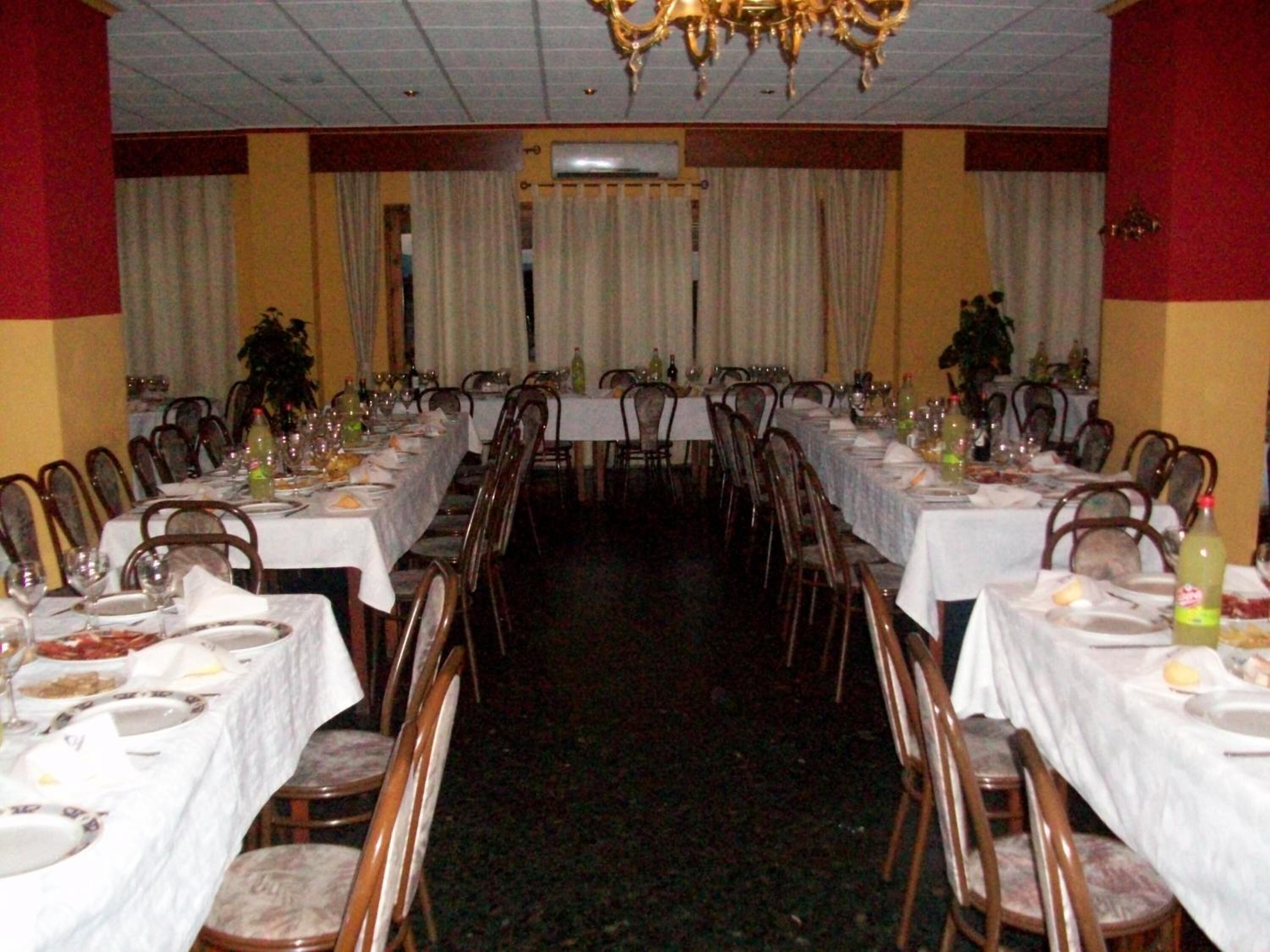 Un salón de banquetes con largas mesas dispuestas para comer, sillas y una araña.