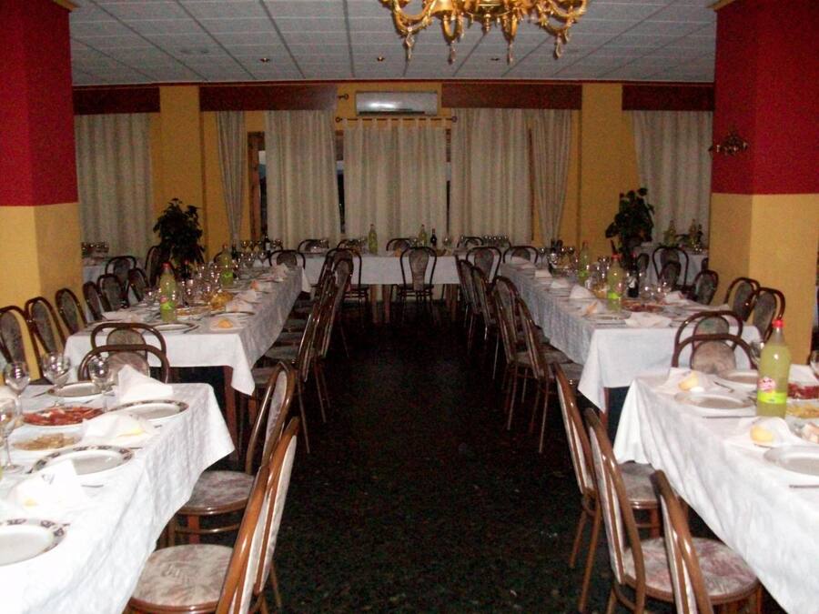 Un salón de banquetes con largas mesas dispuestas para comer, sillas y una araña.