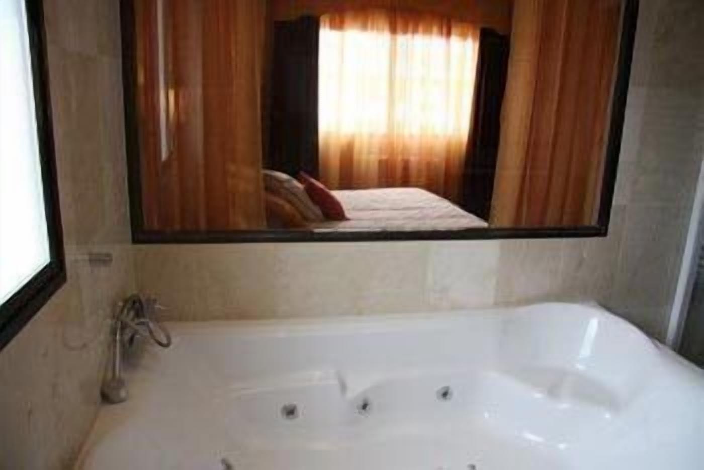 A bathroom with a large bathtub, a mirror, and a window with curtains.