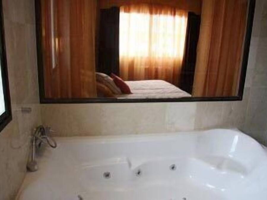 Un baño con una bañera grande, un espejo y una ventana con cortinas.