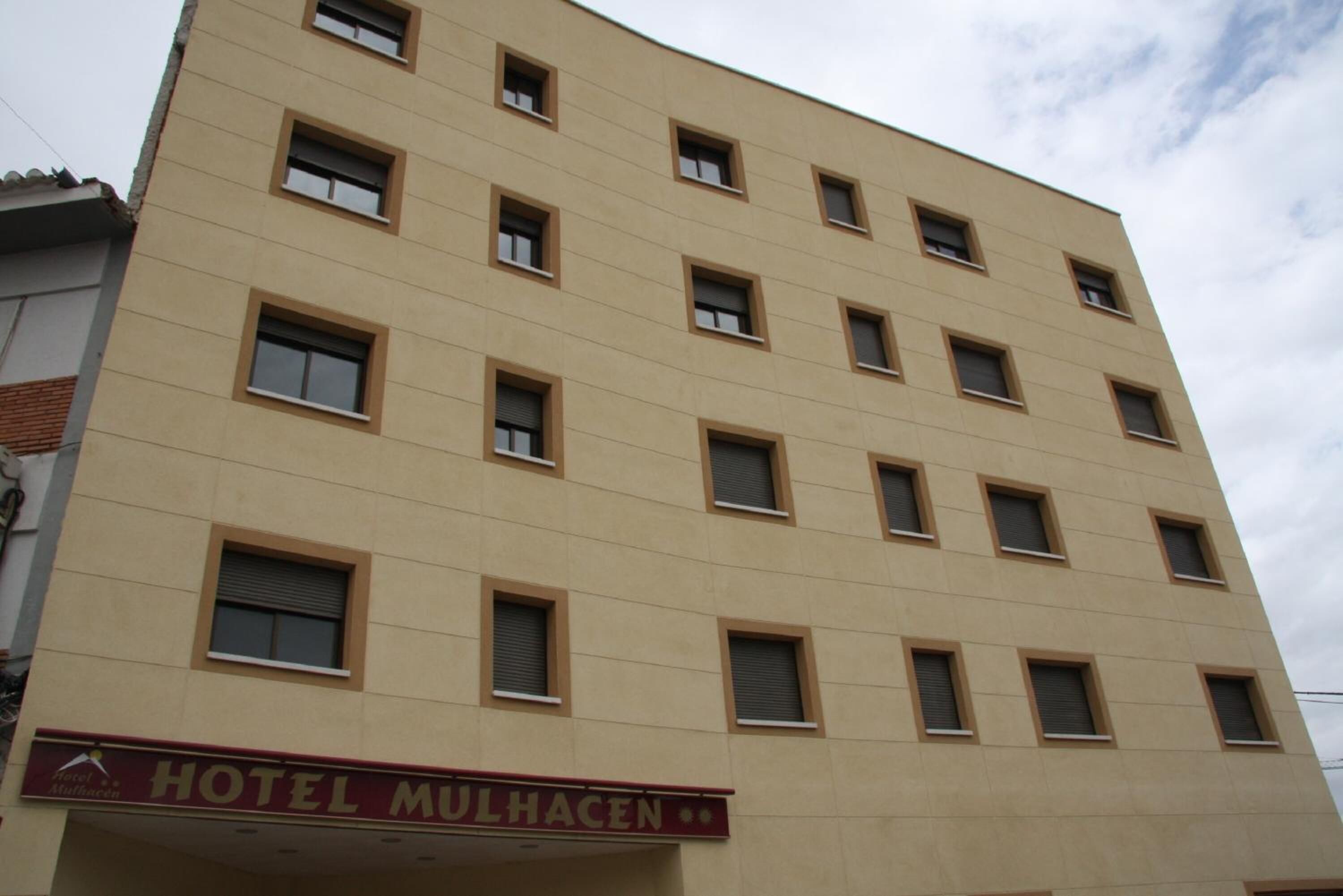 A multi-story hotel building with a beige facade and multiple windows. The hotel's name, "HOTEL MULHACEN," is visible on the ground floor.