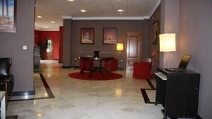 Eine Hotelhalle mit Marmorboden, roten Stühlen um einen Tisch und einem Schreibtisch mit Computer.
