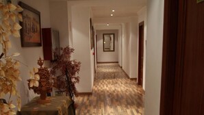 Ein Hotel-Flur mit Holzboden in Schachbrettmuster, einem Esstisch mit Tischdecke, Stühlen und einer Blumenvase.