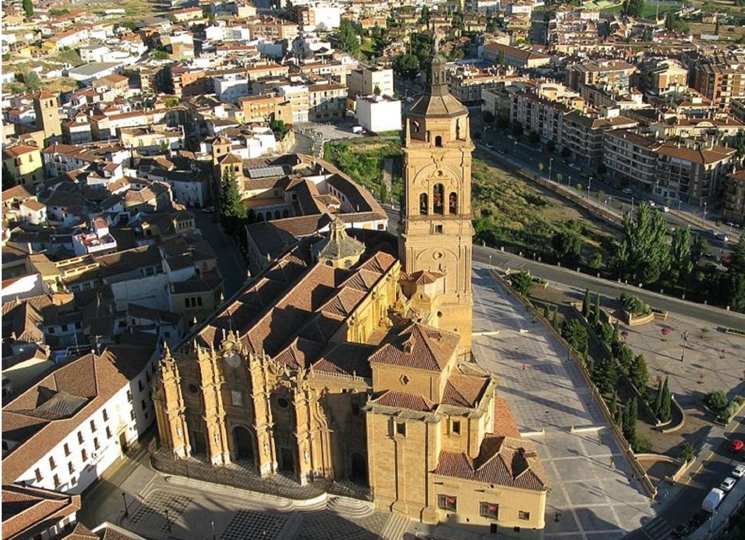 Una iglesia histórica con una imponente torre campanario, rodeada por una plaza y edificios colindantes.