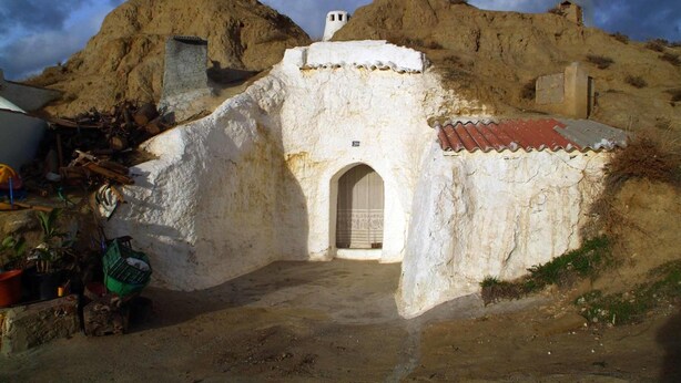 Ein rustikales Gebäude mit weißer Fassade, einem Bogenportal und einem kleinen Glockenturm.
