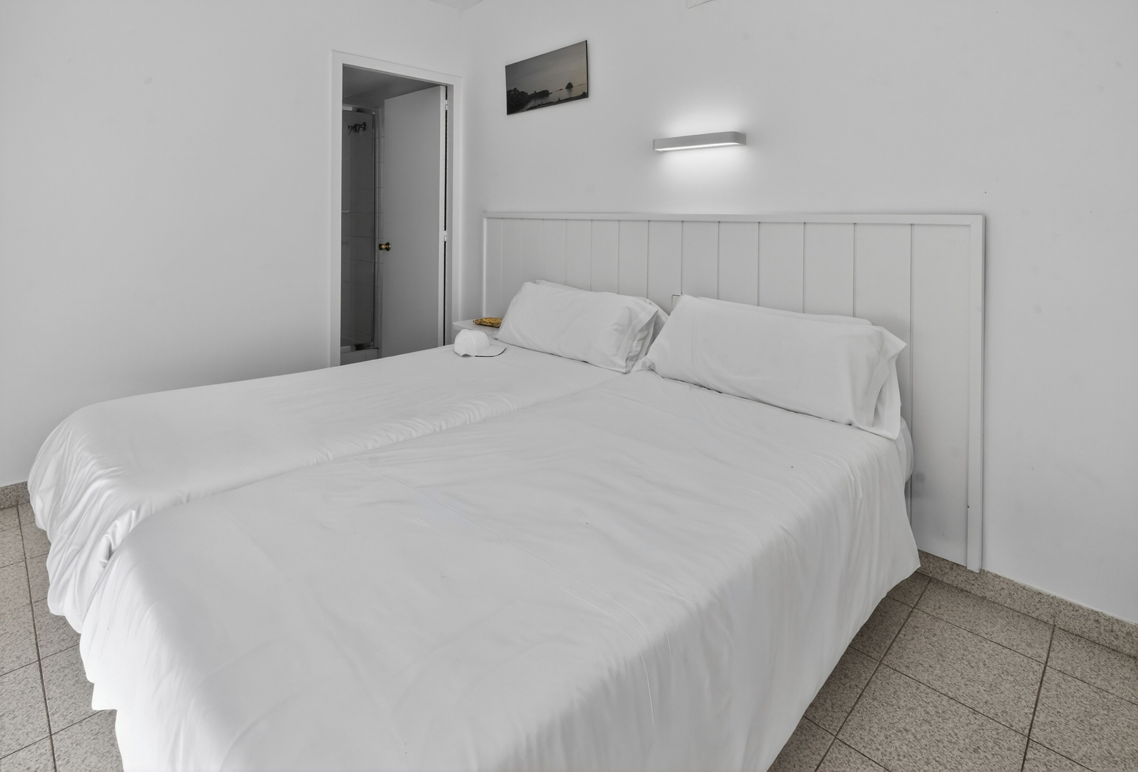 Een hotelkamer met een groot bed, een nachtkastje, een wandlamp en een deur naar een badkamer.