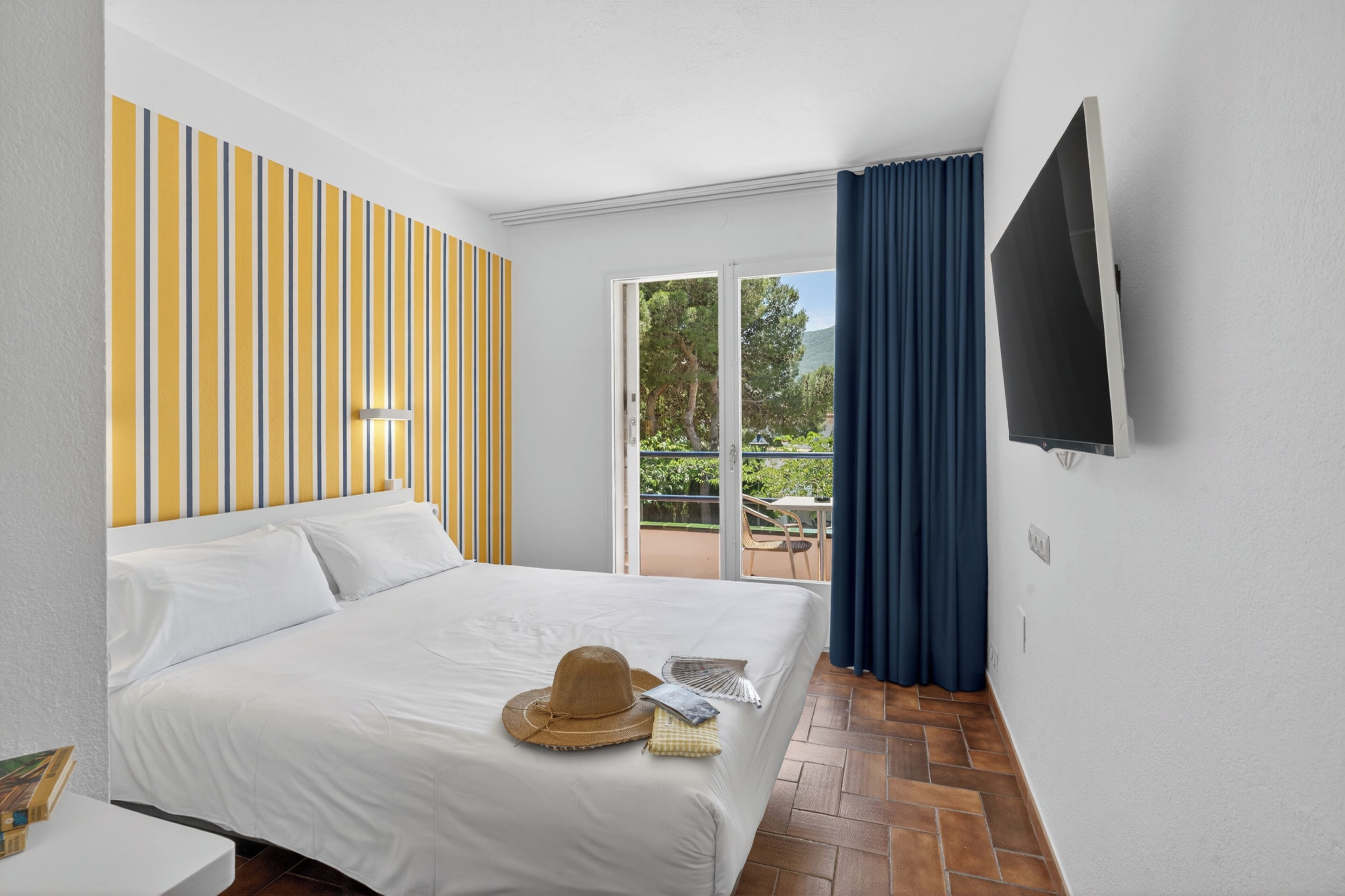 Una camera d'albergo con un letto, una TV, un balcone con tavolo e sedie, e una parete a righe.