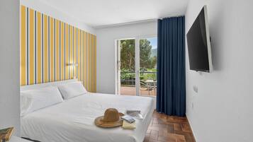 Habitación de hotel con cama, televisión, balcón con mesa y sillas, y pared a rayas.