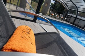 A poolside chair with a towel, a glass balustrade, and a view of a swimming pool. - Hotel del Prado (Puigcerda)