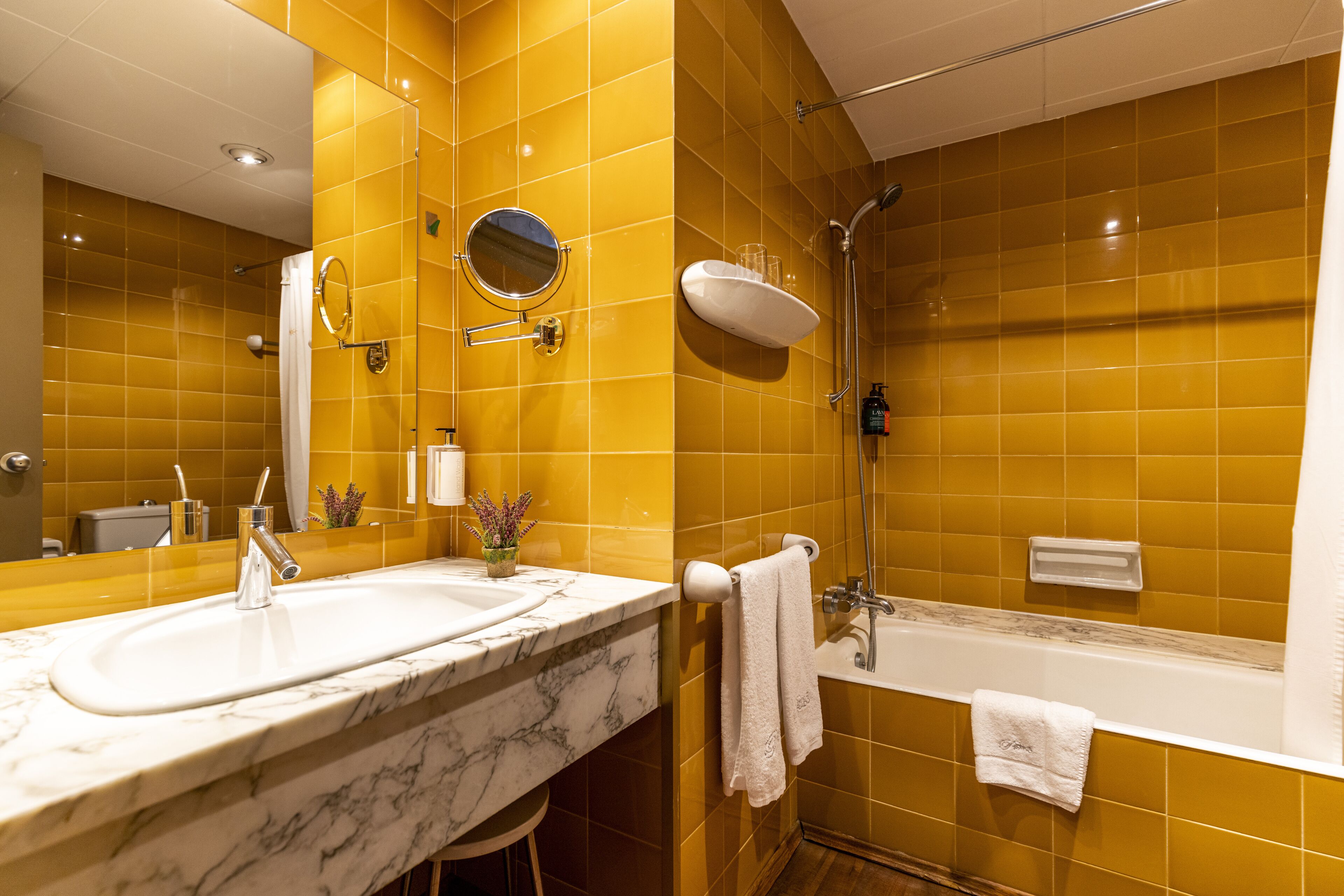 Un baño con azulejos amarillos, un lavabo con encimera de mármol, un espejo, una ducha y una bañera.