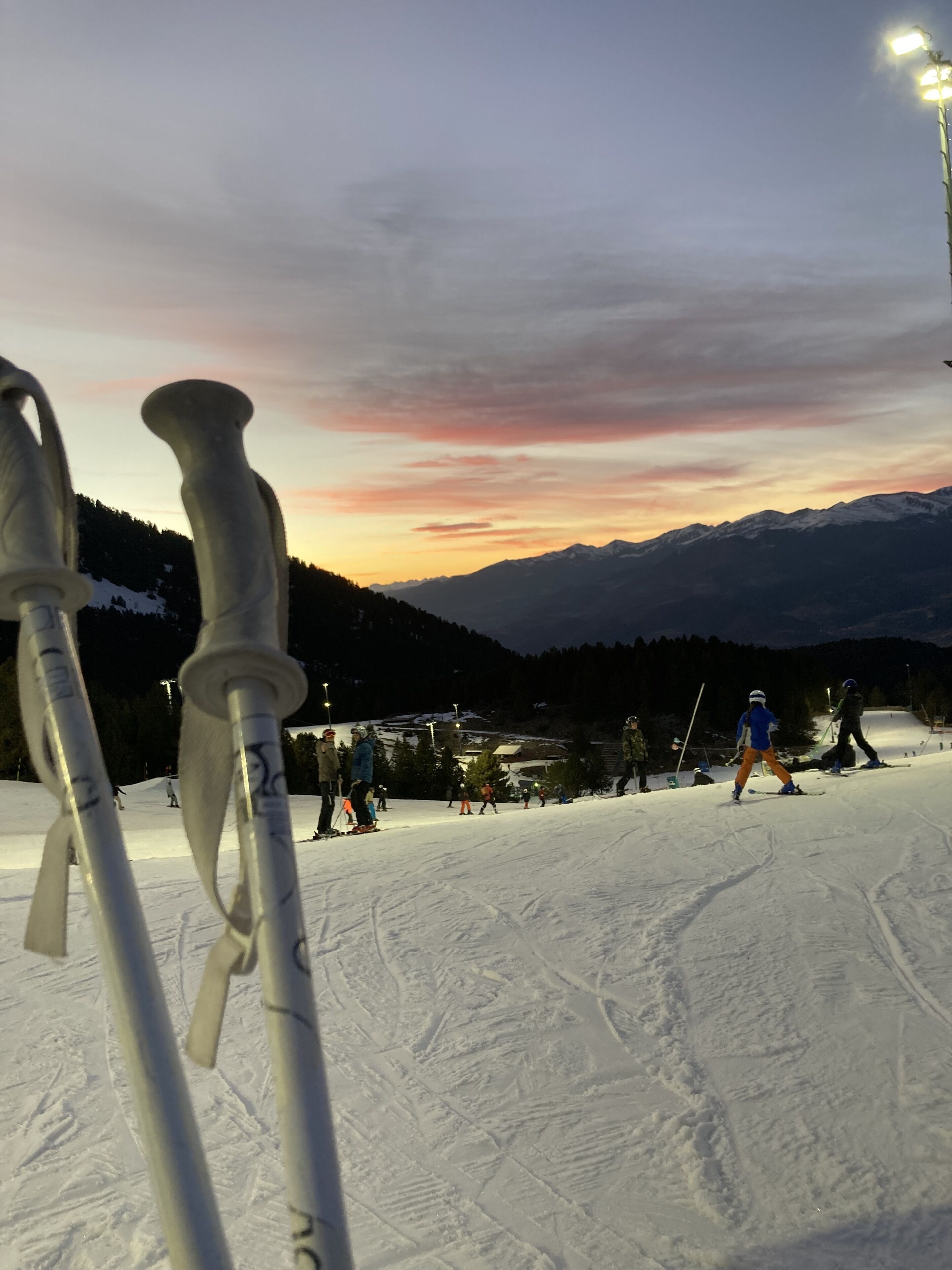 A ski slope with skiers and a sunset in the background.
