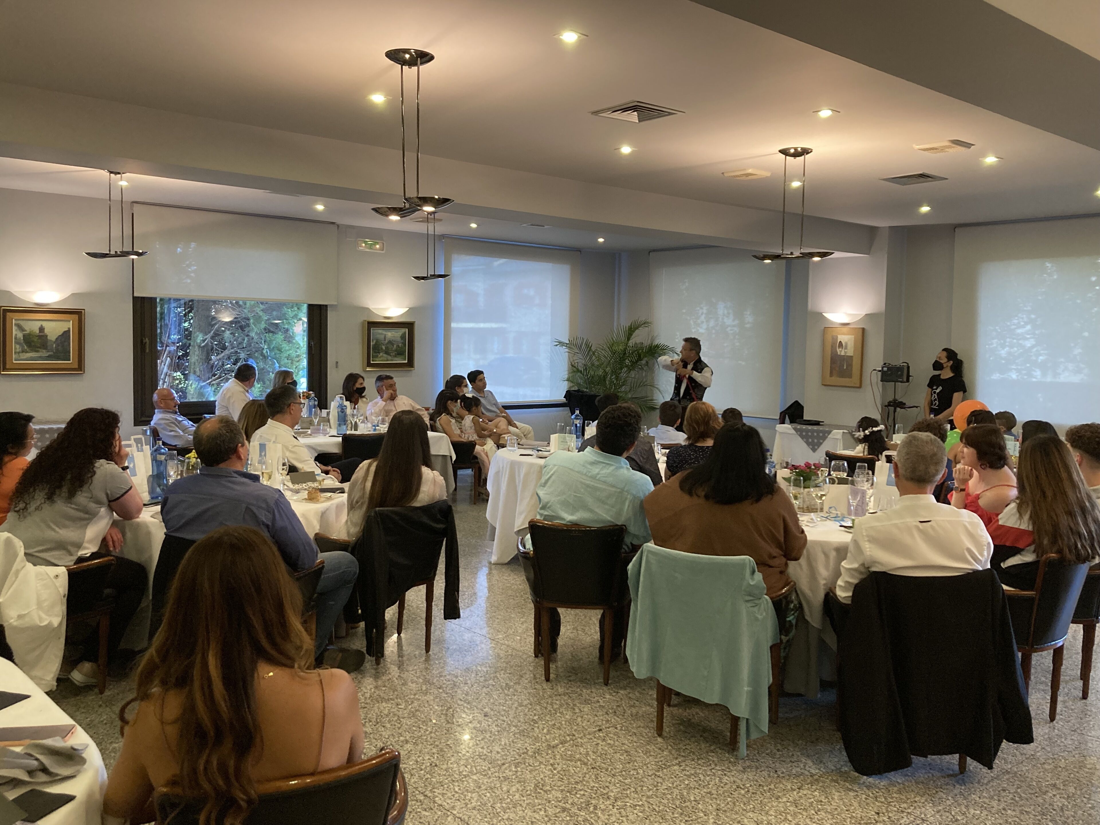 Un salón de conferencias con mesas redondas y sillas, una pantalla de proyector y un orador al frente.