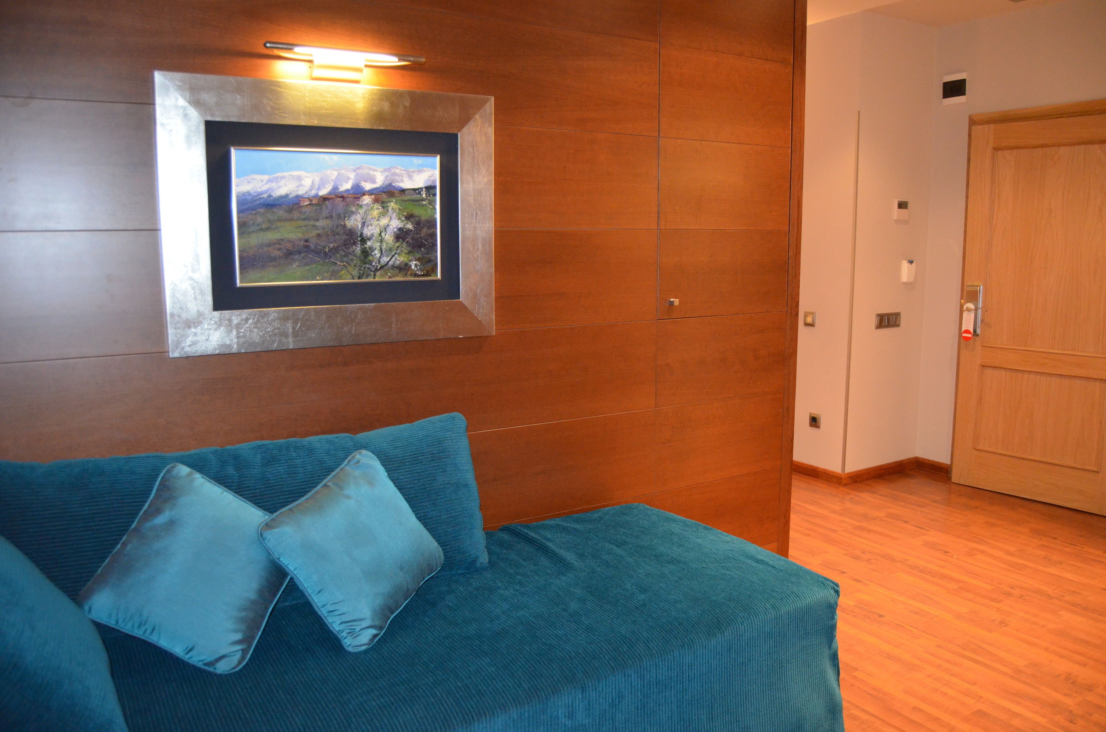 Una habitación con piso de madera, un sofá azul con cojines, un cuadro enmarcado en la pared y una puerta de madera.