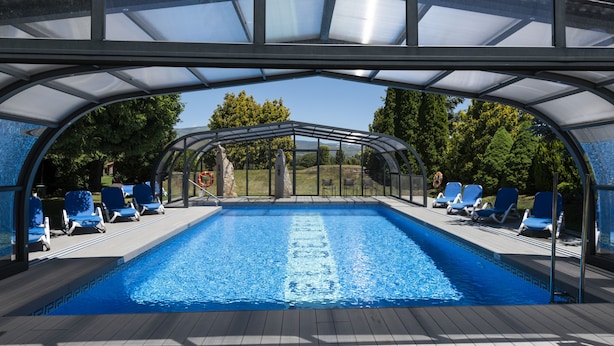 A swimming pool with a glass enclosure, surrounded by lounge chairs and a view of trees. - Hotel del Prado (Puigcerda)