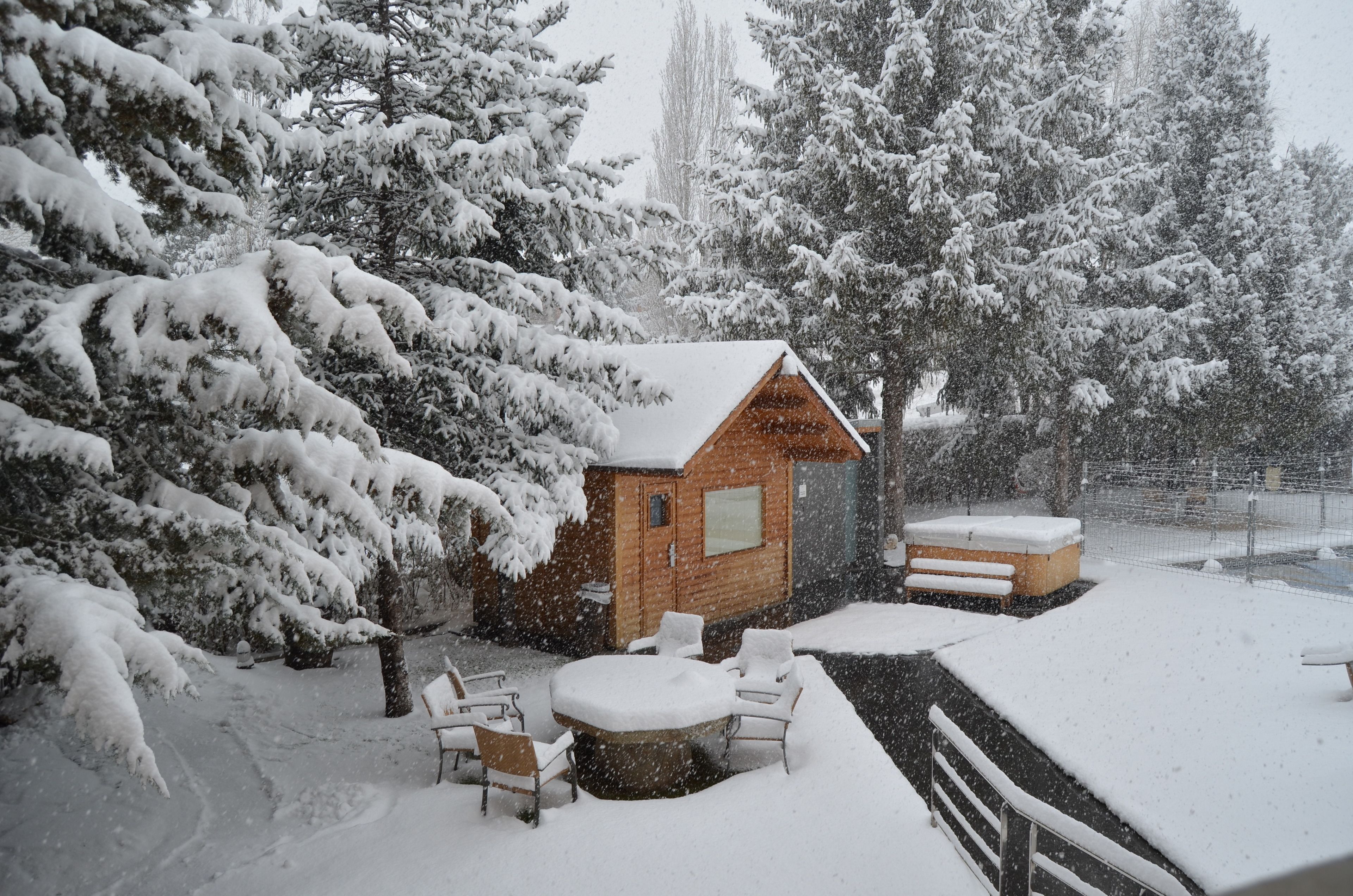 Een houten blokhut met een bubbelbad en een terras, omringd door met sneeuw bedekte bomen.