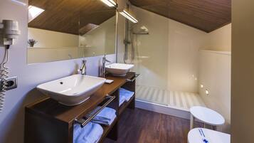 Een moderne badkamer met een houten plafond, een grote spiegel, een wastafel, een douche en een klein tafeltje.