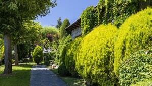 A pathway flanked by neatly trimmed hedges and trees, leading to a stone building with a sloped roof. - Hotel del Prado (Puigcerda)
