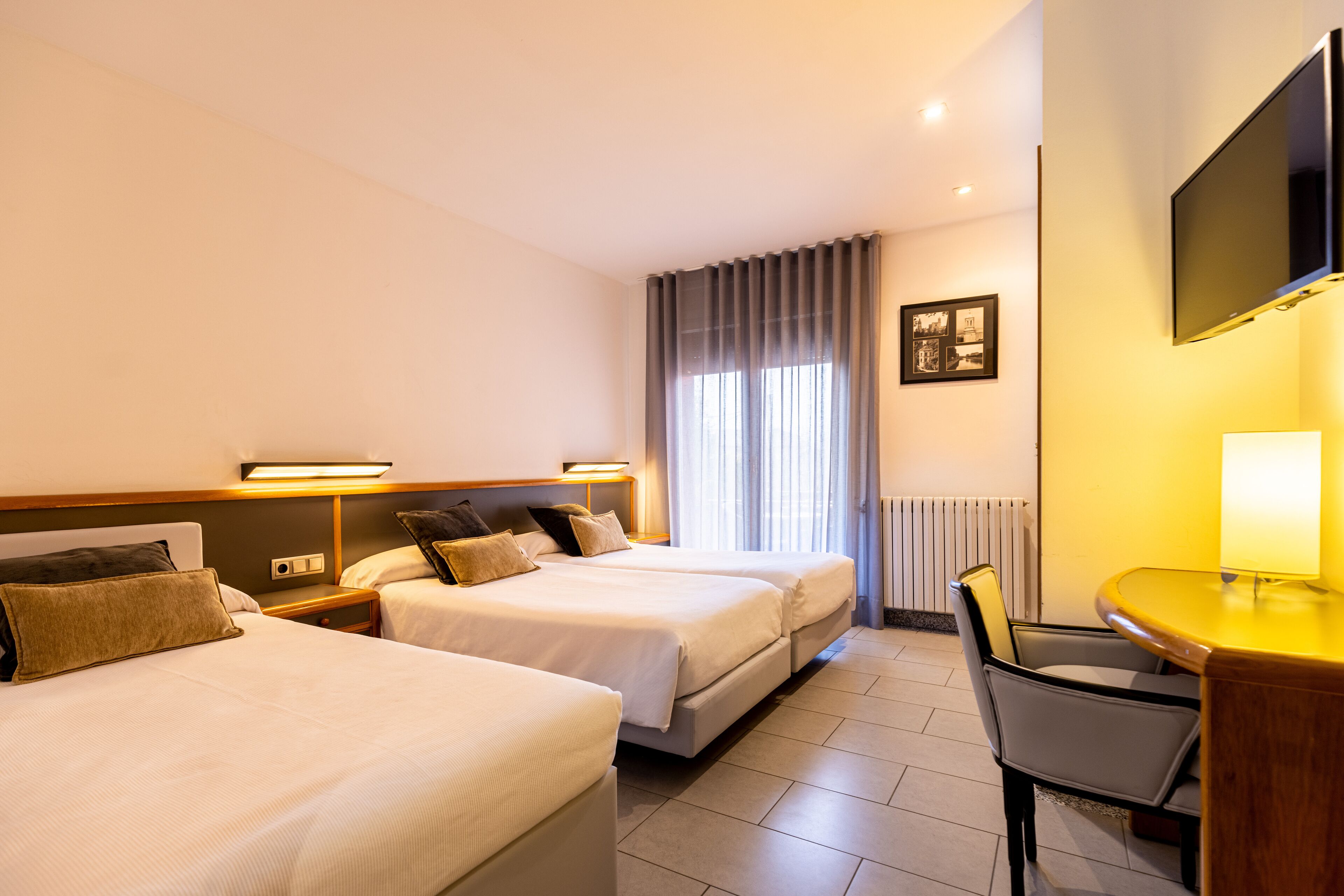Een hotelkamer met twee bedden, een bureau, een stoel, een televisie en een raam met gordijnen.