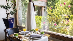 A dining table set with breakfast items, a potted plant, and a view of a garden through a window. - Hotel del Prado (Puigcerda)