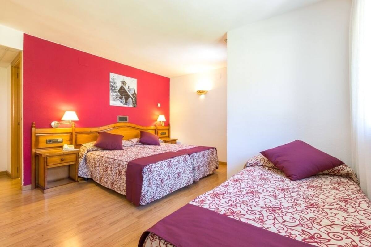 Un dormitorio con dos camas, una pared roja y suelo de madera.