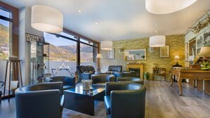 A spacious living room with a large window, a fireplace, and a dining area with a table and chairs. - Hotel Eth Solan (Vielha e Mijaran)