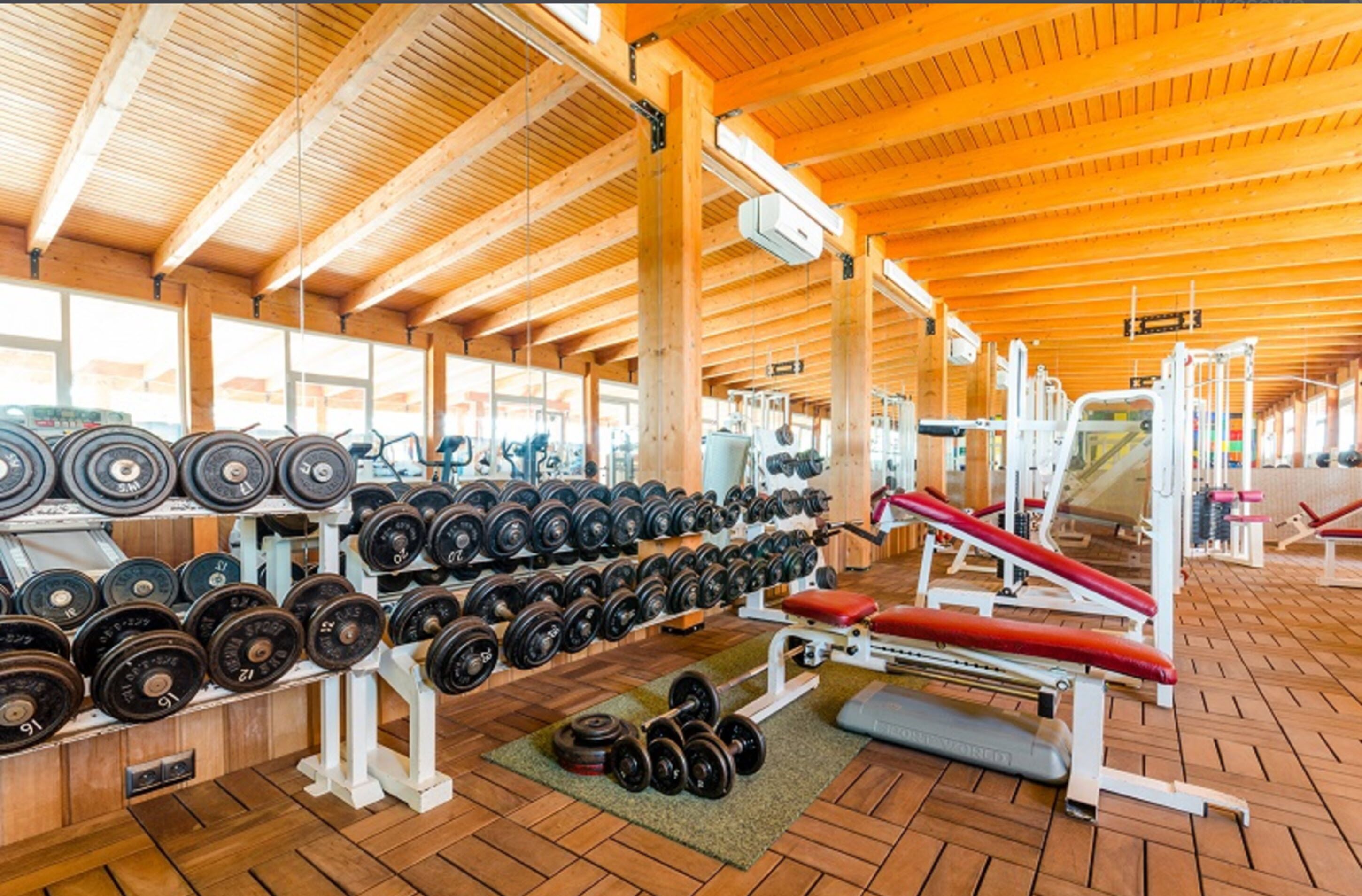 Un gimnasio con vigas de madera, estantes para pesas y equipo de ejercicio.