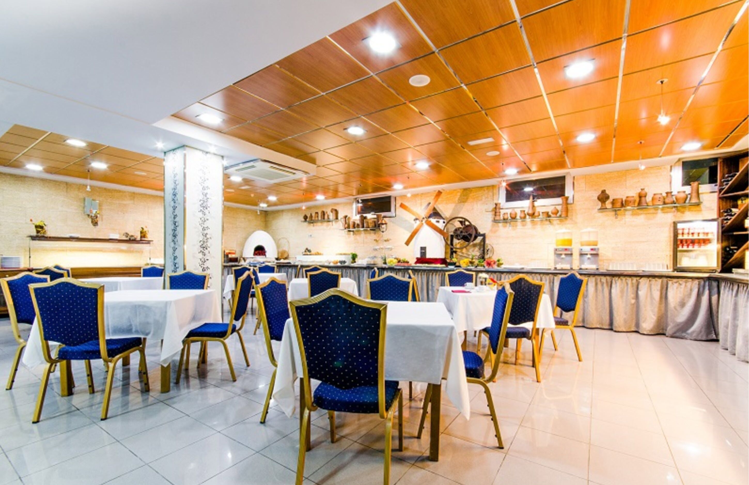 A restaurant with wooden ceiling, blue chairs, and white tables.