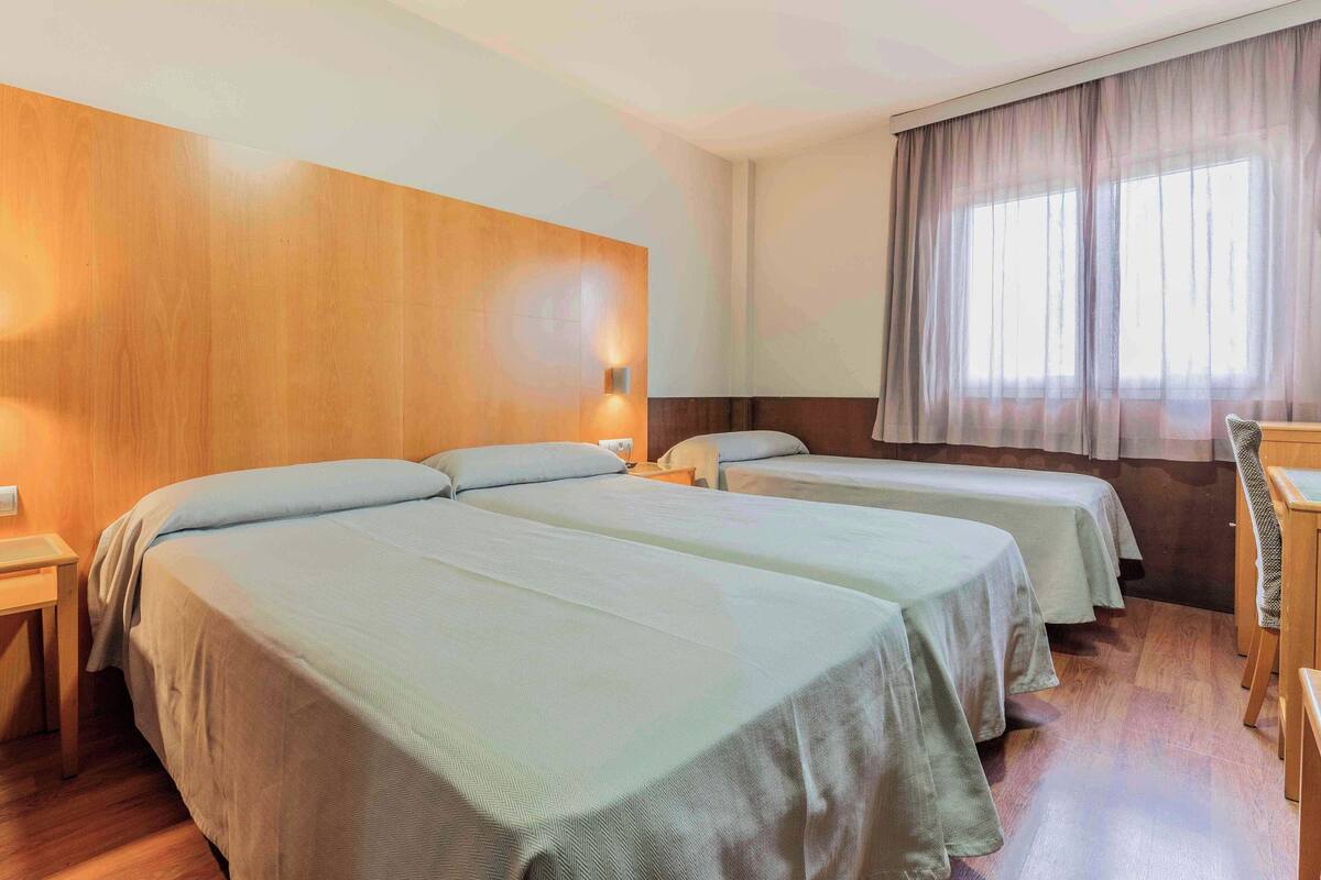 Een hotelkamer met twee eenpersoonsbedden, houten wanden, een raam met gordijnen en een nachtkastje met een lamp.