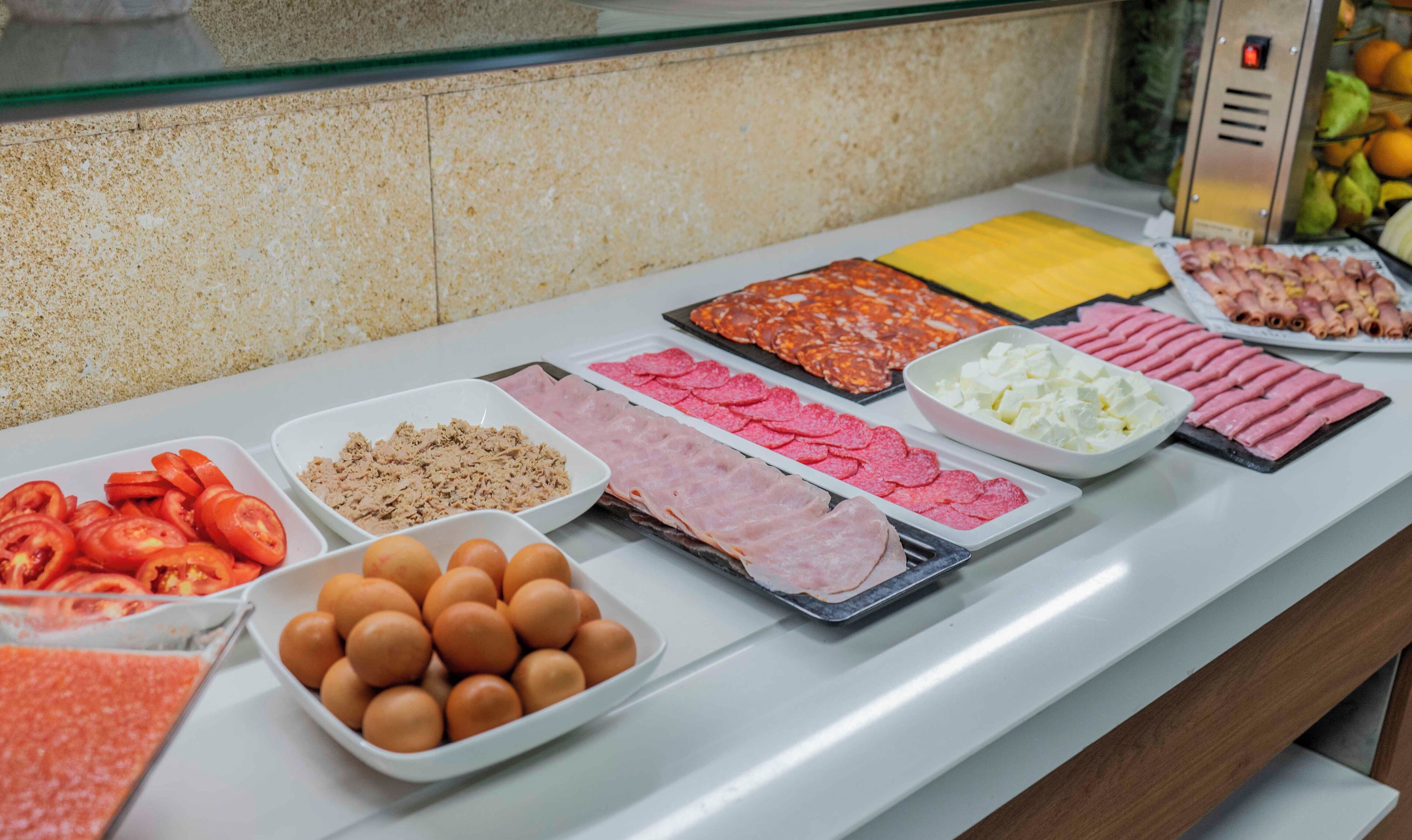 A buffet with various food items including sliced tomatoes, eggs, and different types of meat.