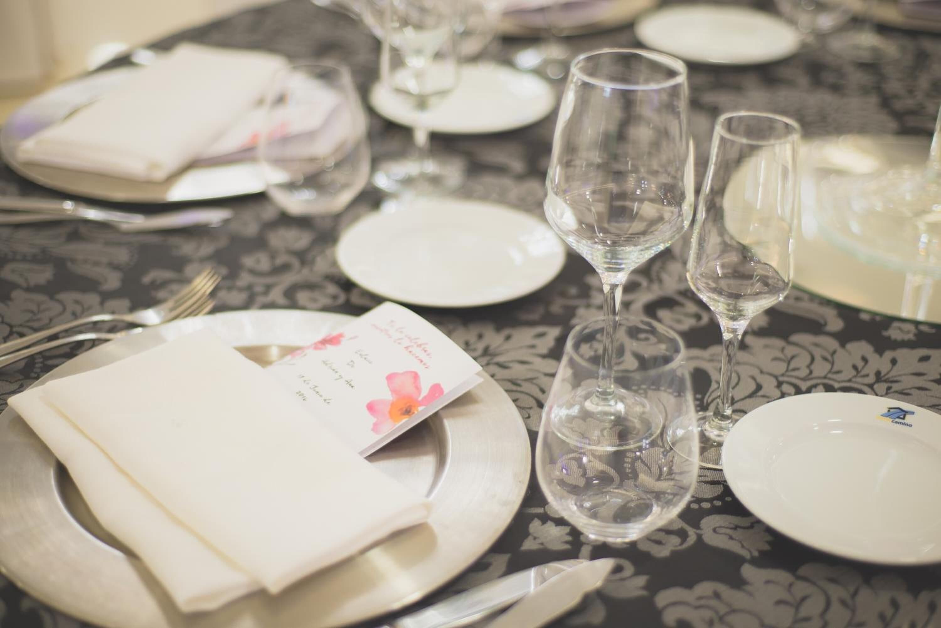 Una mesa preparada para una comida, con platos, cubiertos y copas de vino.