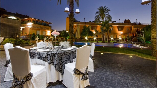 An outdoor dining area with a table set for six, surrounded by palm trees and a pool. - Checkin Camino de Granada (Granada)